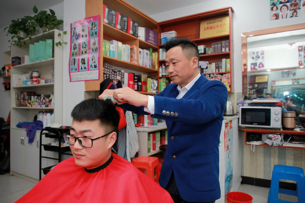 图为截肢手术半年后,胡之勤丢掉拐杖站着理发。